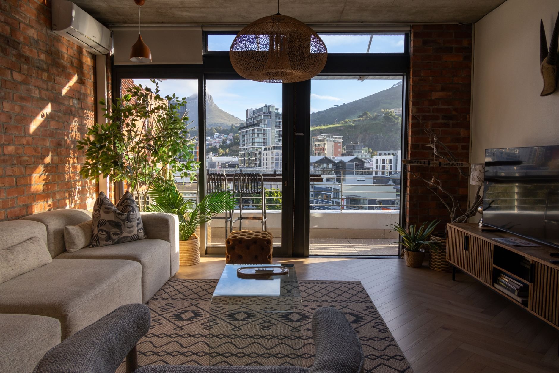 Cozy living room interior with neutral tones, plants, and a view of Cape Town's mountains through large windows.