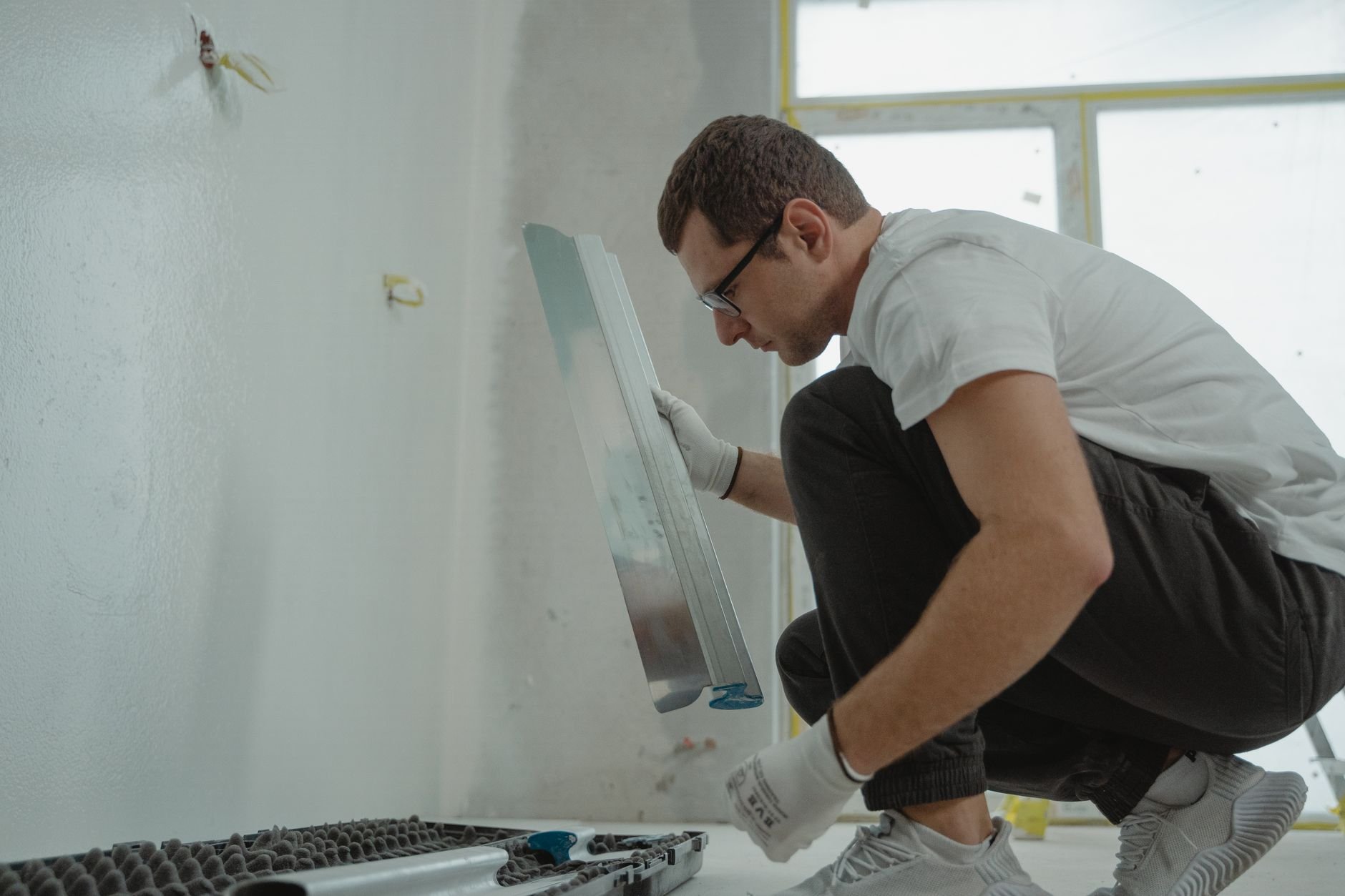 A man in a white shirt plastering and finishing interior home renovation walls.